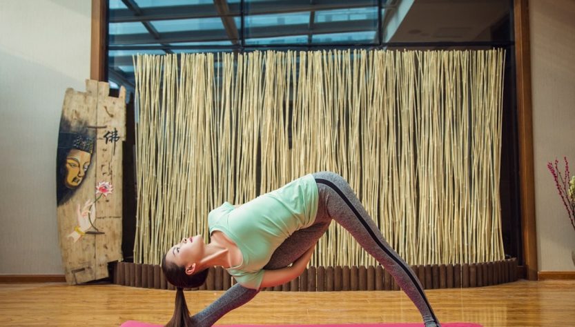 woman in green tank top and gray leggings doing yoga